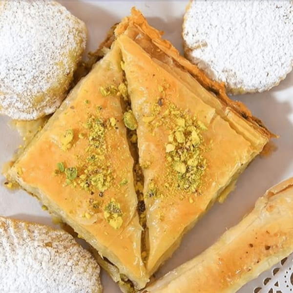 Two pieces of baklava with pistachios and powdered sugar cookies on a white plate.
