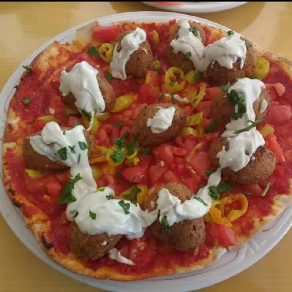 Dalia's Mediterranean pizza with falafel, diced tomatoes, yellow peppers, and a creamy white sauce.
