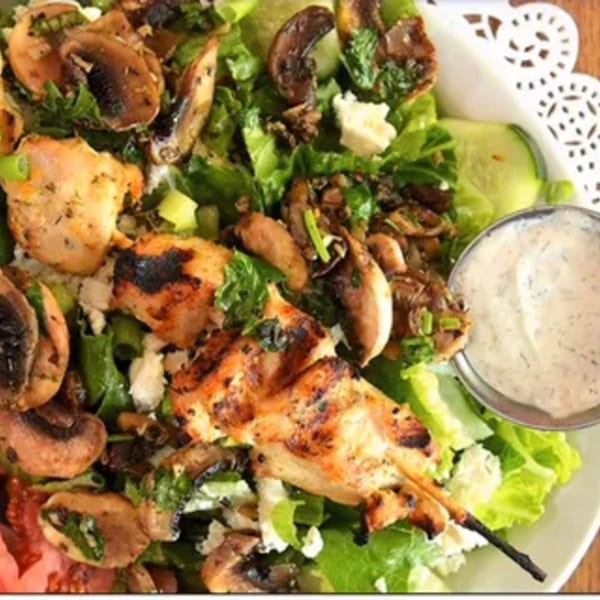A Dalia's Mediterranean salad with grilled chicken skewers, mushrooms, feta, and dressing.